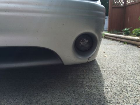 2002 Pontiac Grand Prix - A close-up, low-angle shot of the lower front bumper of a silver car, showing a fog light and some minor damage on the bumper's edge. The c…