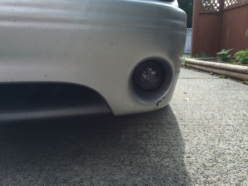 Close-up of a silver car's front bumper with fog light and scuff mark.