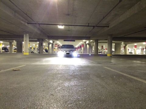 2002 Pontiac Grand Prix - A silver sedan with its headlights on is parked in a dimly lit, multi-level parking garage. The car is centered in the frame, facing the ca…