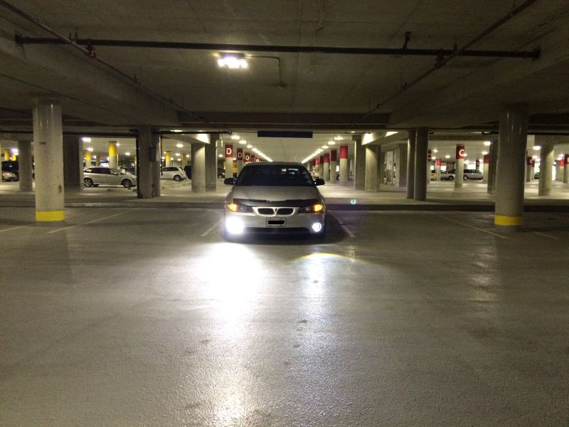 Silver Pontiac Grand Prix in a parking garage with headlights on.
