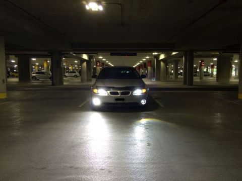 2002 Pontiac Grand Prix - A silver Pontiac Grand Prix is parked in a dimly lit parking garage with its headlights on, illuminating the wet concrete floor.