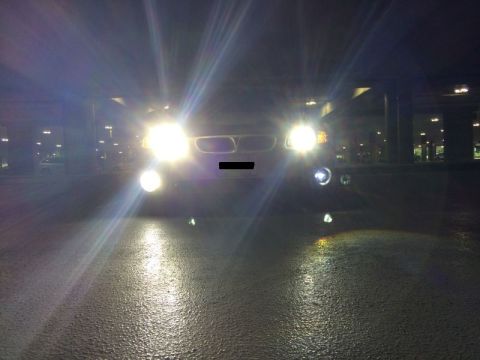 2002 Pontiac Grand Prix - The front of a white sedan with its headlights on, parked on a wet asphalt surface at night. The car is viewed from a low angle, directly i…