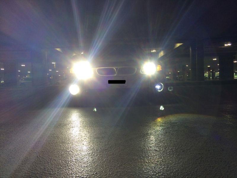 Front view of a white sedan with headlights on, parked on wet asphalt at night.