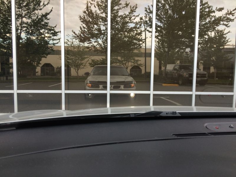 Reflection of a silver sedan's front end in a building's windows.
