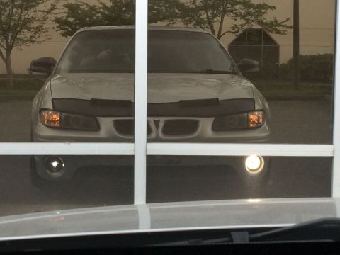 2002 Pontiac Grand Prix - The front view of a silver sedan is visible through a window, with a car bra covering the hood. Fog lights are illuminated on the lower fro…