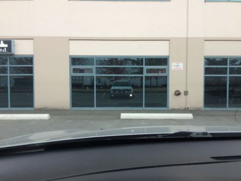 2002 Pontiac Grand Prix - A silver van is reflected in the large windows of a commercial building. The van is parked in a lot in front of the building.