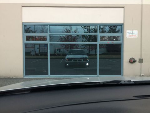 2002 Pontiac Grand Prix - A silver sedan is reflected in the large windows of a commercial building. The car is parked in a lot facing the building, with its headlig…