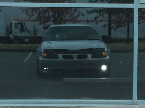 2002 Pontiac Grand Prix - The front view of a silver Pontiac Grand Prix is reflected in a window. The car has its headlights and fog lights on and a black car bra co…