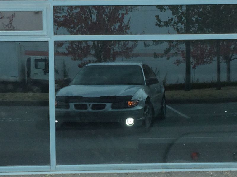 Silver sedan's front end seen through a reflective window.