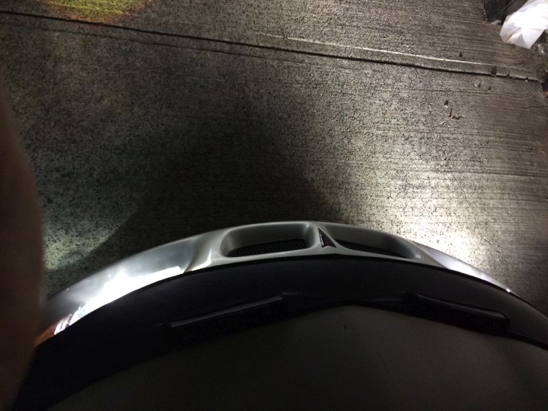 Front view of a dark car at night with headlights on, showing a silver hood scoop.