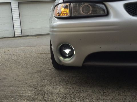 2002 Pontiac Grand Prix - A close-up, low-angle shot of the front bumper and driver's side headlight of a silver Pontiac Grand Prix. The driver's side fog light is i…
