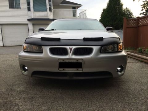 2002 Pontiac Grand Prix - Front view of a silver Pontiac Grand Prix with a black bra on the hood. The car is parked in a driveway in front of a white house.