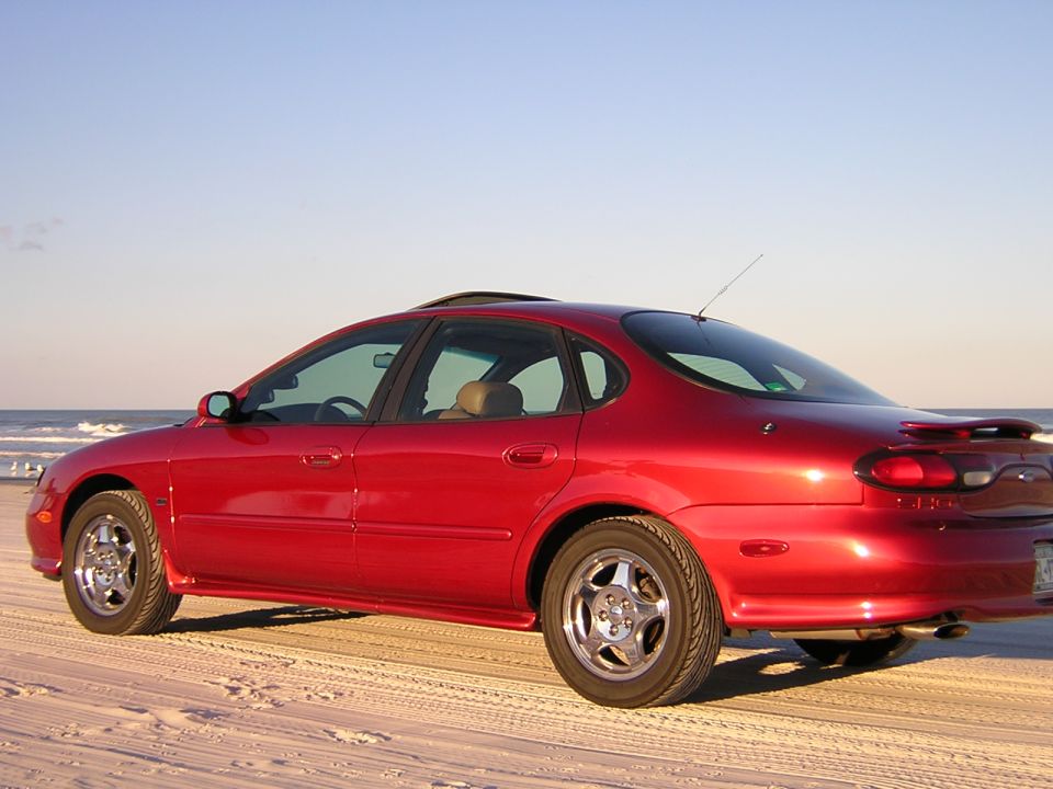 Red 1997 Ford Taurus parked on a sandy beach with the ocean in the background
