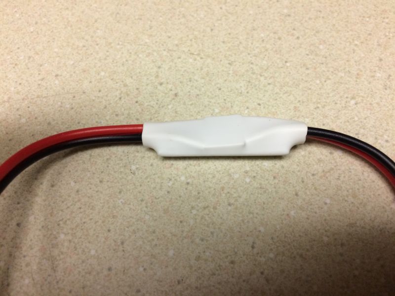 White plastic casing over a red and black wire splice on a speckled surface.