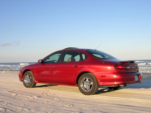 1997 Ford Taurus - Red 1997 Ford Taurus parked on the beach with waves in the background.