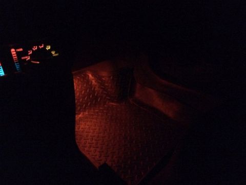 2002 Pontiac Grand Prix - The interior of a car at night shows a diamond plate floor mat illuminated by red light, with the dashboard climate controls visible in the…