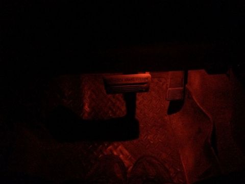 2002 Pontiac Grand Prix - The interior of a vehicle is shown with red ambient lighting. Visible are the brake pedal, the parking brake lever with the text "ANTI-LOCK…