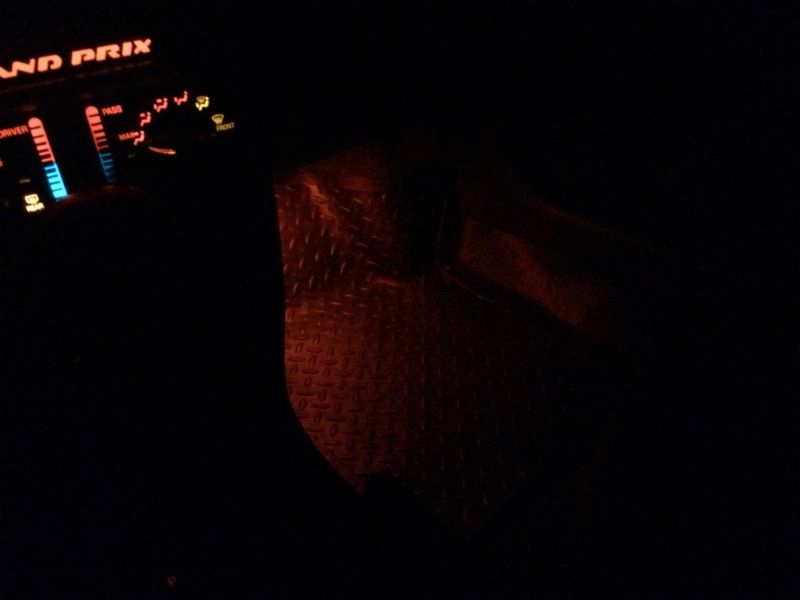 Car interior at night showing illuminated dashboard and diamond plate floor mat.