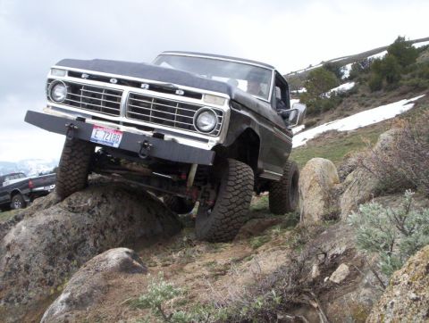 1978 Ford Bronco - A modified black Ford truck navigates a rocky incline with snow patches visible on the hillside.