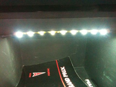 2002 Pontiac Grand Prix - A strip of LED lights illuminates a black surface, casting a bright glow. In the foreground, a portion of a black document with red accents…