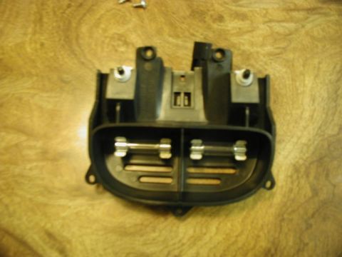 2002 Pontiac Grand Prix - A black plastic automotive fuse box with two glass fuses installed is shown on a wooden surface. The fuse box has metal contacts visible on…