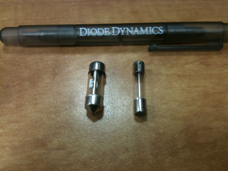 Two glass fuses and a pen with "DIODE DYNAMICS" text on a wooden surface.