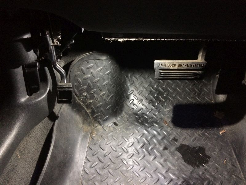 Interior view of car floor showing brake and accelerator pedals and a rubber floor mat.