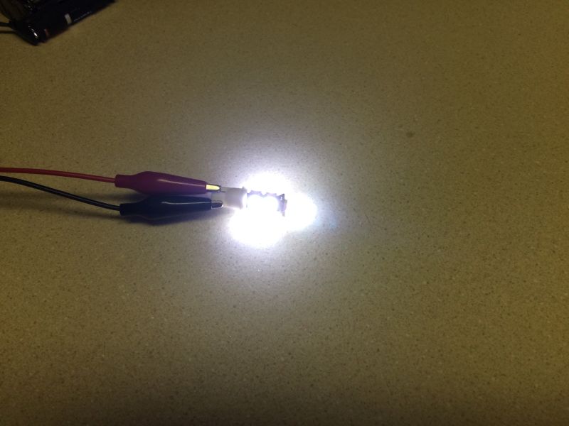 Close-up of a bright white LED powered by alligator clips.