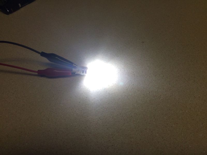 Close-up of a bright white LED light connected to alligator clip wires.