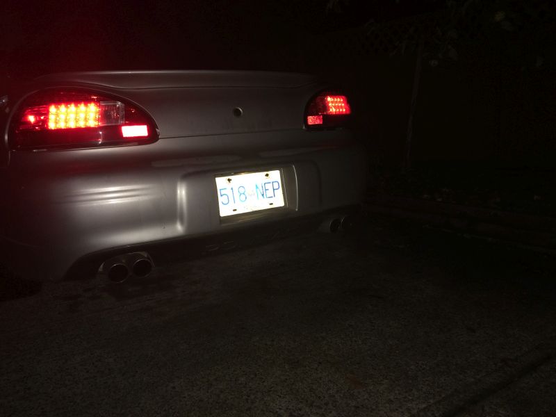 Rear view of a silver 2002 Pontiac Grand Prix at night with illuminated taillights and dual exhaust.