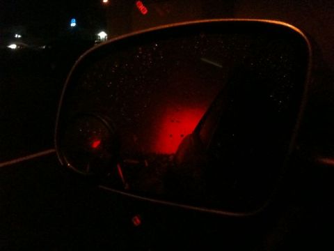 2002 Pontiac Grand Prix - A close-up shot of a car's side mirror at night, reflecting red taillights and a blurry road. The mirror surface is speckled with water dro…