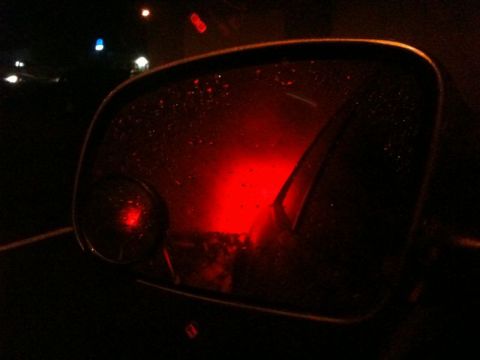 2002 Pontiac Grand Prix - A car's side mirror reflects a bright red taillight at night, with visible raindrops on the mirror's surface.