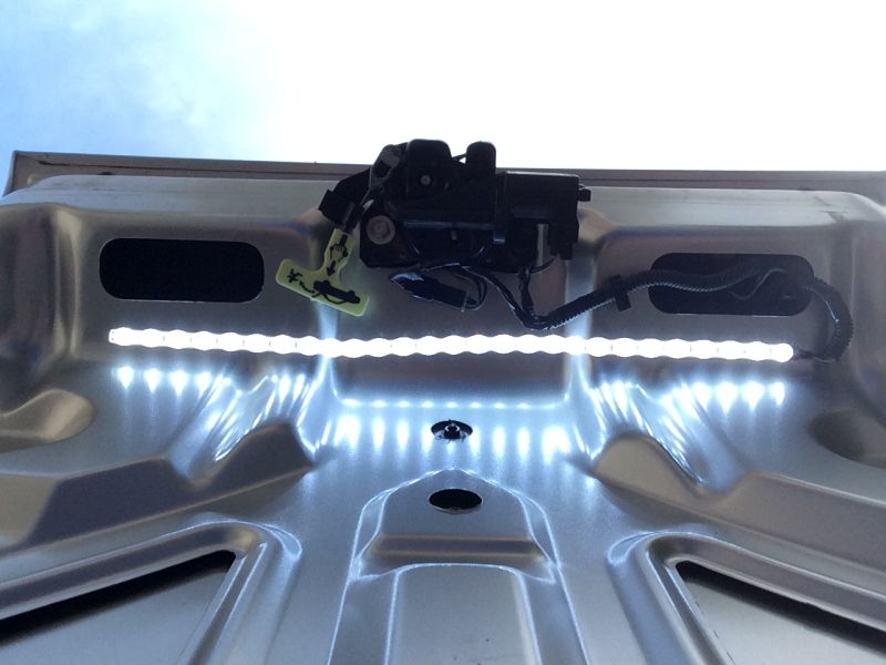 Underside of a car trunk lid with LED lights and latch mechanism.