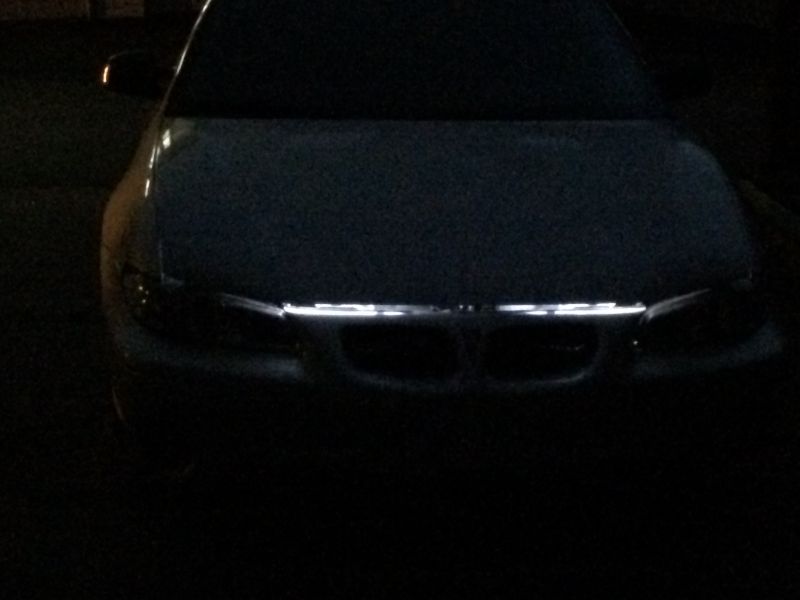 Front of a dark car with white LED strip lighting on the grille at night.