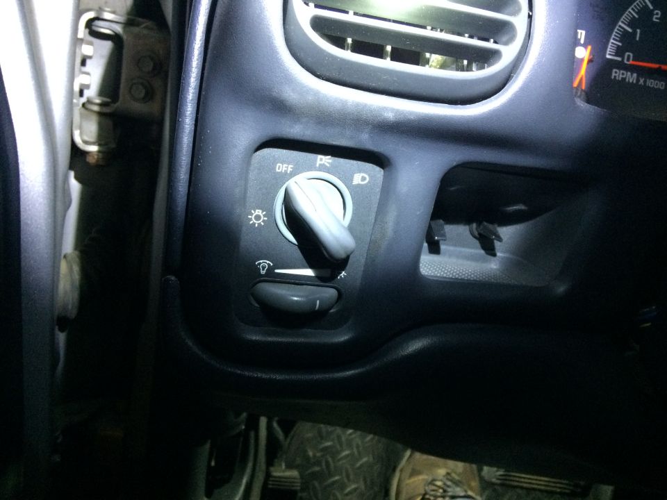 Close-up of car dashboard showing headlight switch and part of RPM gauge.