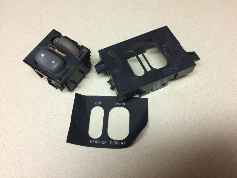 Disassembled head-up display control module with gray buttons and slider, and a separate label.