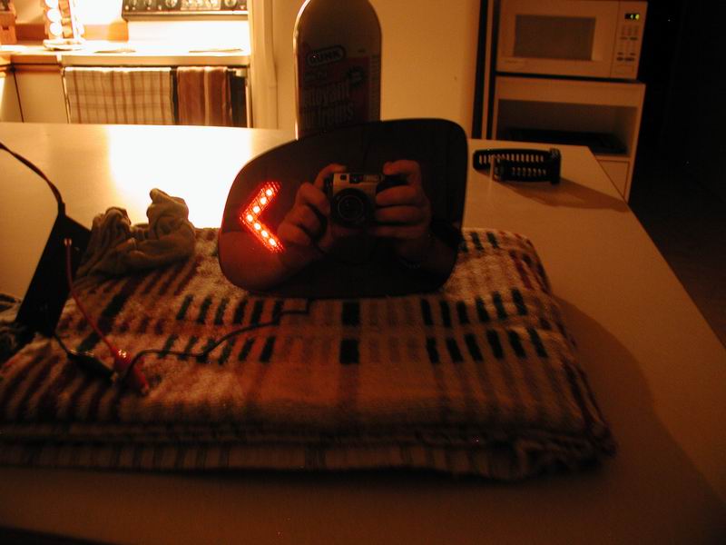 Modified side mirror with illuminated red arrow turn signal, reflecting a camera.