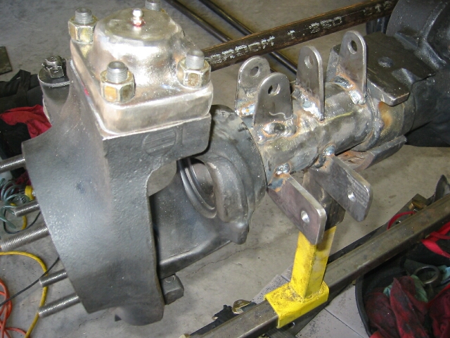 Solid front axle knuckle with freshly welded suspension bracket tabs, supported on a stand in a garage