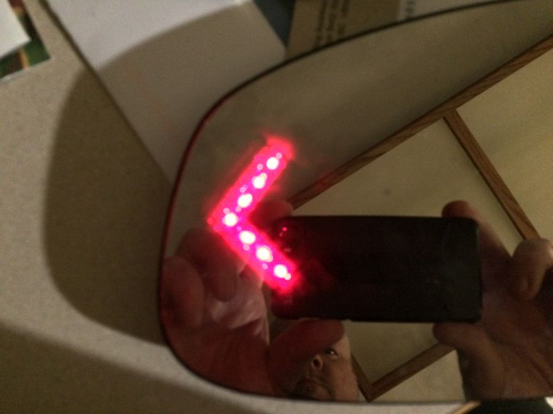 Red LED arrow indicator reflected in a car's side mirror.