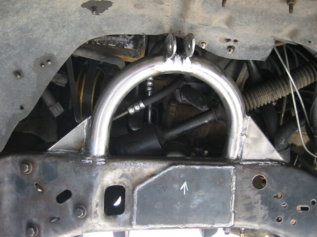 Custom welded bare-steel shock hoop with gussets on a truck frame inside the front wheel well