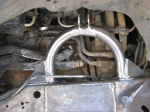 1994 Ford Bronco - Close-up view of a custom-welded suspension part on a vehicle frame, with engine components in the background.