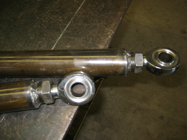 Two polished rod ends with heim joints and jam nuts on a metal bench