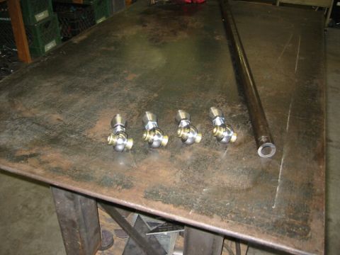 1994 Ford Bronco - Four rod ends and a metal tube are laid out on a workbench, suggesting automotive parts.