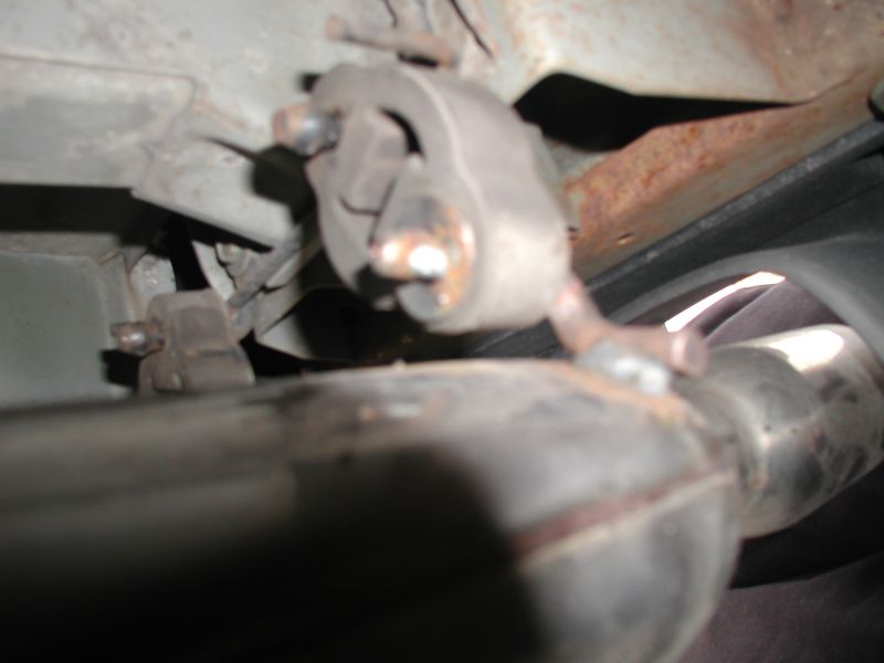 Underside of a vehicle showing exhaust pipe and rusty mounting brackets.