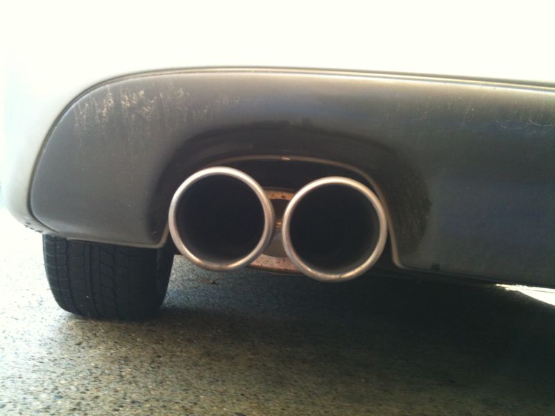 Close-up of a car's dual exhaust pipes and rear bumper.