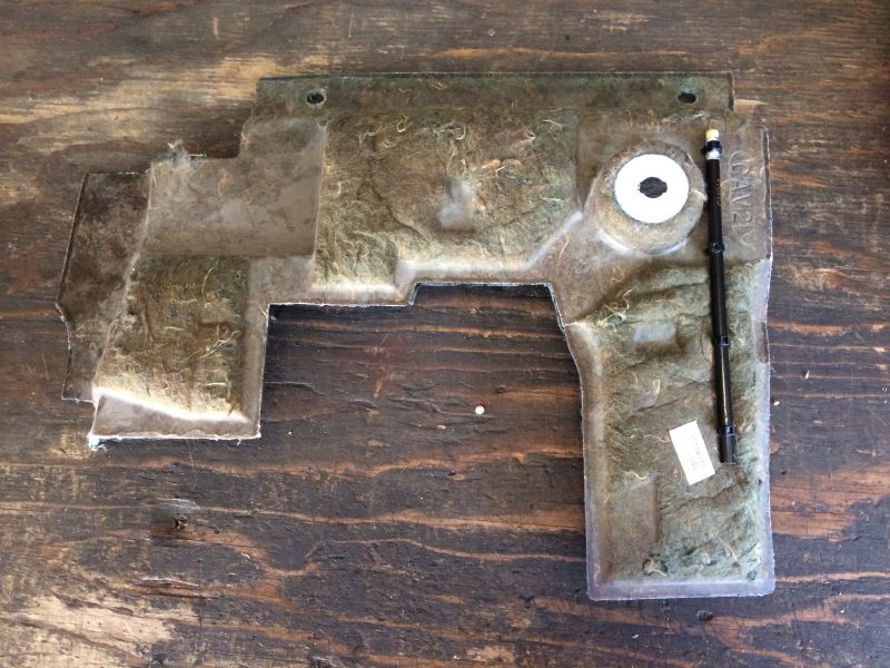 Car part, likely an underbody shield, on a wooden surface.