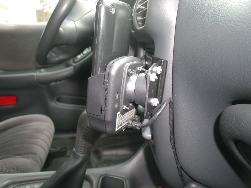 GPS device mounted on car dashboard with metal bracket and wiring.