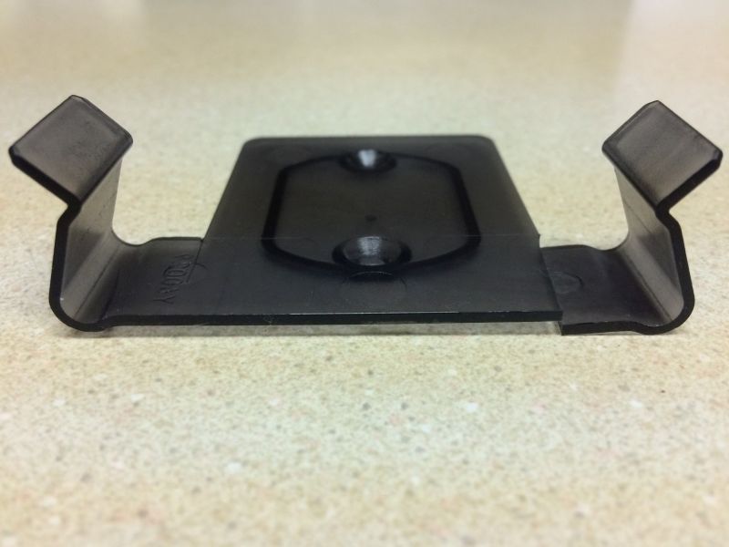 Black plastic bracket with prongs and faint text "200AY" on a speckled surface.