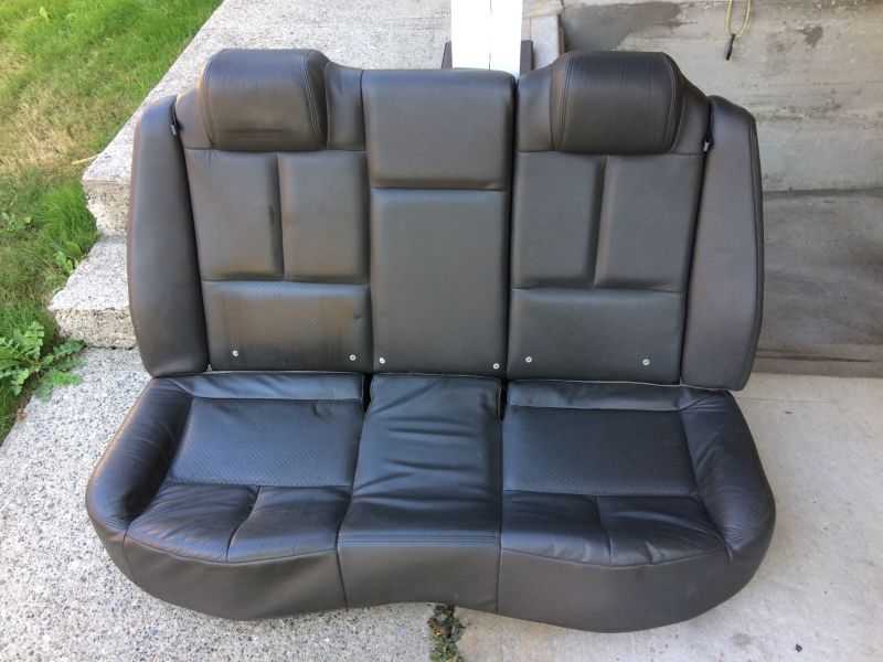 Black leather rear car seat assembly with three headrests and perforated sections.