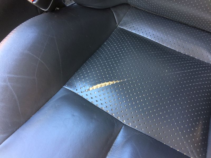 Damaged black leather car seat with scratches and a tear.